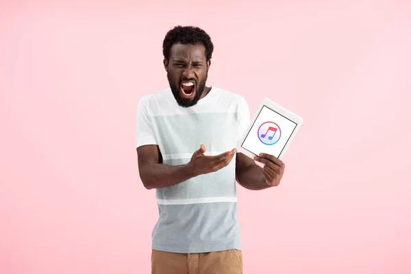 Київ, Україна-17 травня 2019: емоційна афроамериканець людина кричав і показуючи цифровий планшет з Apple Music App, ізольований на рожевому — стокове фото
