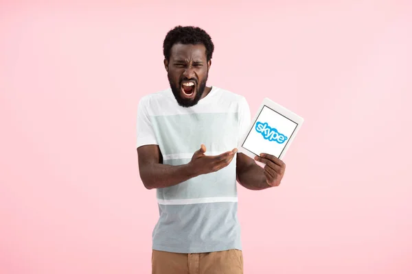 KYIV, UKRAINE - MAY 17, 2019: emotional african american man shouting and showing digital tablet with skype app, isolated on pink — Stock Photo