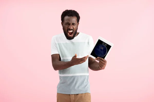 KYIV, UKRAINE - MAY 17, 2019: emotional african american man shouting and showing digital tablet, isolated on pink — Stock Photo