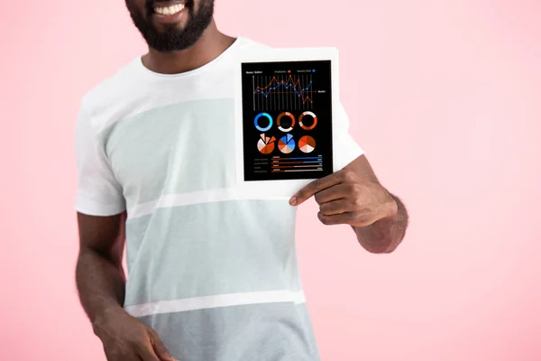 Recortado vista del hombre afroamericano sonriente mostrando tableta digital con aplicación de infografía, aislado en rosa - foto de stock