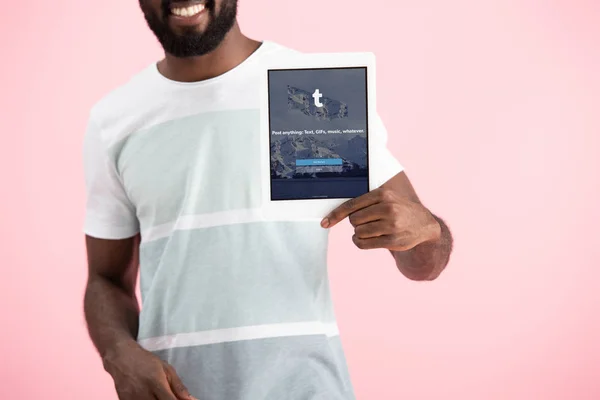 KYIV, UKRAINE - 17 MAI 2019 : vue recadrée d'un homme afro-américain montrant une tablette numérique avec application tumblr, isolé sur rose — Photo de stock