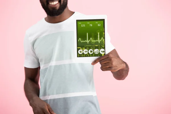 Recortado vista de sonriente afroamericano hombre mostrando tableta digital con aplicación de salud, aislado en rosa - foto de stock