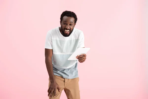 Rindo homem afro-americano usando tablet digital isolado em rosa — Fotografia de Stock