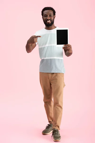 Lächelnder afrikanisch-amerikanischer Mann zeigt auf digitales Tablet mit leerem Bildschirm isoliert auf rosa — Stockfoto