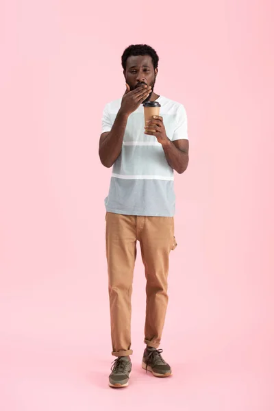 Cansado afro-americano bocejando e segurando café para ir, isolado em rosa — Fotografia de Stock