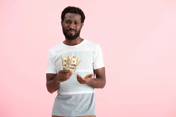 Homem afro-americano confuso segurando notas de dólares, isolado em rosa — Fotografia de Stock
