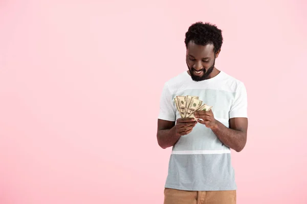 Hombre afroamericano feliz sosteniendo billetes de dólares, aislado en rosa - foto de stock