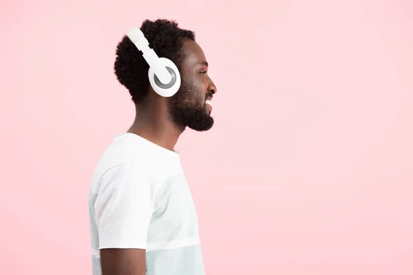 Barbudo afro-americano ouvindo música com fones de ouvido, isolado em rosa — Fotografia de Stock
