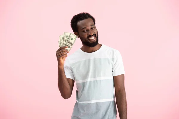 Sonriente hombre afroamericano sosteniendo billetes de dólares, aislado en rosa - foto de stock