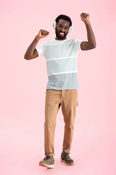 Heureux homme afro-américain danser et écouter de la musique avec écouteurs, isolé sur rose — Photo de stock