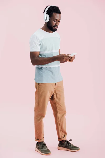 Afro-americano ouvindo música com fones de ouvido e smartphone, isolado em rosa — Fotografia de Stock
