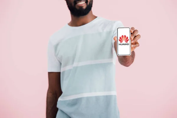 КИЕВ, УКРАИНА - 17 мая 2019 года: обрезанный вид африканского американца, показывающего смартфон с приложением huawei, изолированным на розовом — стоковое фото