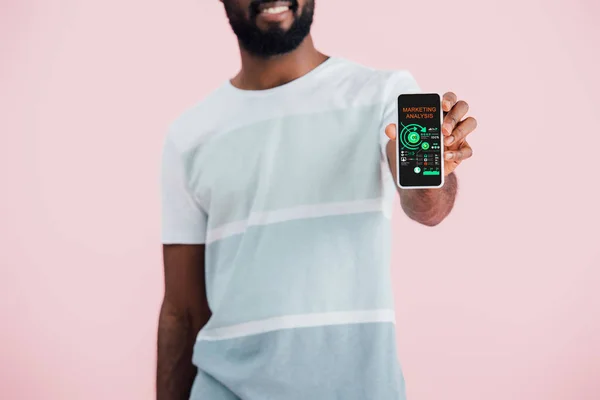 Vista cortada do homem afro-americano mostrando smartphone com aplicativo de análise de marketing, isolado em rosa — Fotografia de Stock