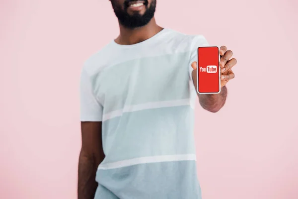 KYIV, UKRAINE - 17 MAI 2019 : vue recadrée d'un homme afro-américain montrant un smartphone avec application youtube, isolé sur rose — Photo de stock