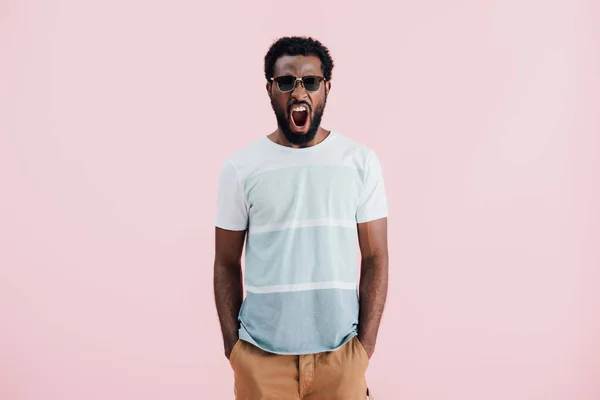 Agresivo africano americano de hombre en gafas de sol gritando aislado en rosa - foto de stock