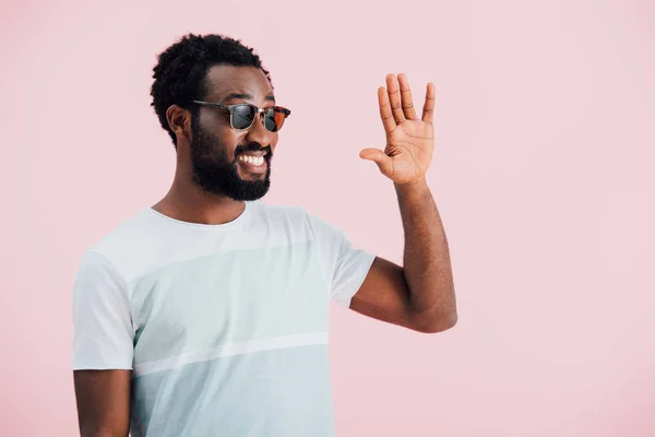 Fröhliche junge afrikanisch-amerikanische Mann mit Sonnenbrille winkt isoliert auf rosa — Stockfoto