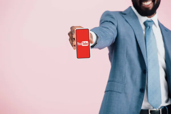 KYIV, UKRAINE - MAY 17, 2019: cropped view of african american businessman in suit showing smartphone with youtube app, isolated on pink — Stock Photo