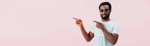 Sorridente afro-americano de homem de óculos de sol apontando para o lado, isolado em rosa — Fotografia de Stock