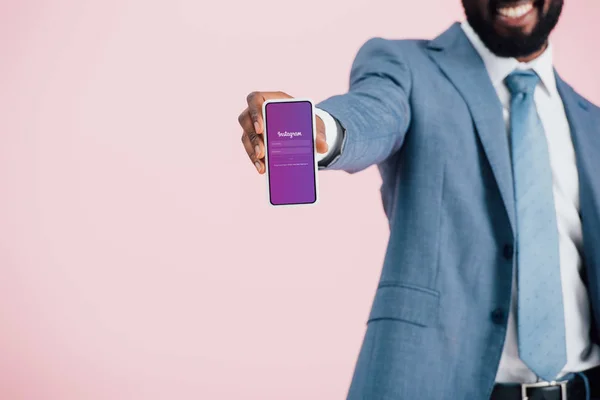 KYIV, UKRAINE - 17 MAI 2019 : vue recadrée d'un homme d'affaires afro-américain en costume montrant un smartphone avec application instagram, isolé sur rose — Photo de stock