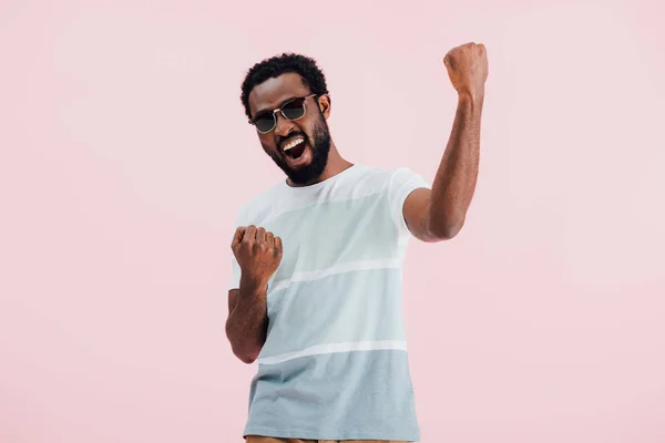 Bem sucedido jovem afro-americano de homem em t-shirt e óculos de sol, isolado em rosa — Fotografia de Stock
