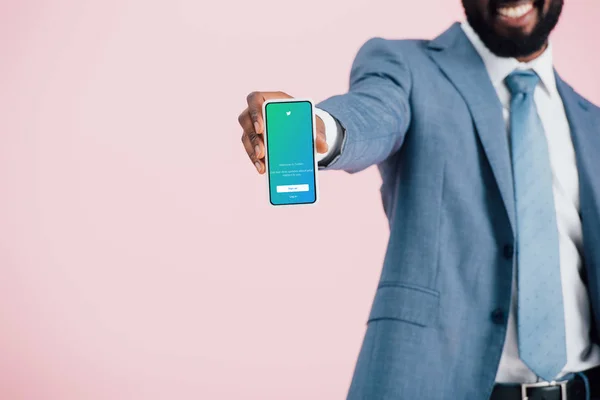 KYIV, UKRAINE - 17 MAI 2019 : vue recadrée d'un homme d'affaires afro-américain en costume montrant un smartphone avec application twitter, isolé sur rose — Photo de stock