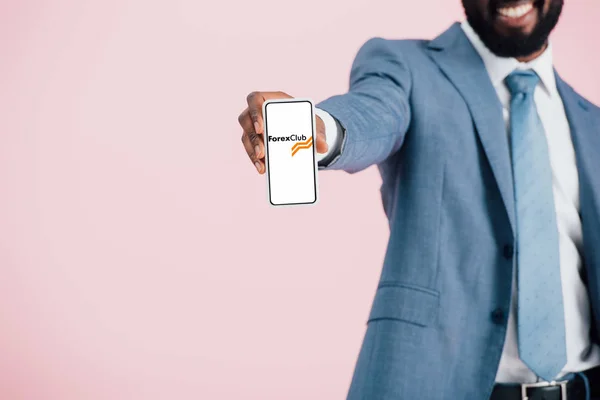 KYIV, UKRAINE - MAY 17, 2019: cropped view of african american businessman in suit showing smartphone with forex club app, isolated on pink — Stock Photo