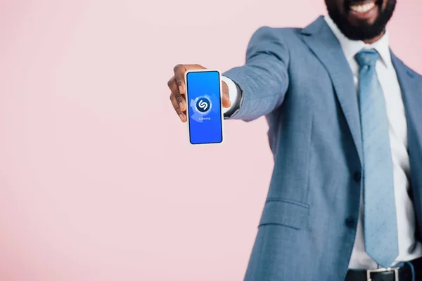 KYIV, UKRAINE - 17 MAI 2019 : vue recadrée d'un homme d'affaires afro-américain en costume montrant un smartphone avec une application shazam, isolé sur rose — Photo de stock