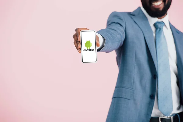 KYIV, UKRAINE - MAY 17, 2019: cropped view of african american businessman in suit showing smartphone with android app, isolated on pink — Stock Photo