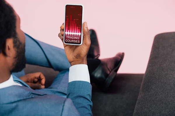 Обрізаний вид афроамериканського бізнесмена, що показує смартфон з торговими курсами, ізольований на рожевому — стокове фото