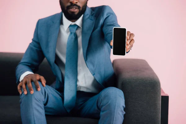 Vista recortada del hombre de negocios afroamericano que muestra el teléfono inteligente con pantalla en blanco, aislado en rosa - foto de stock