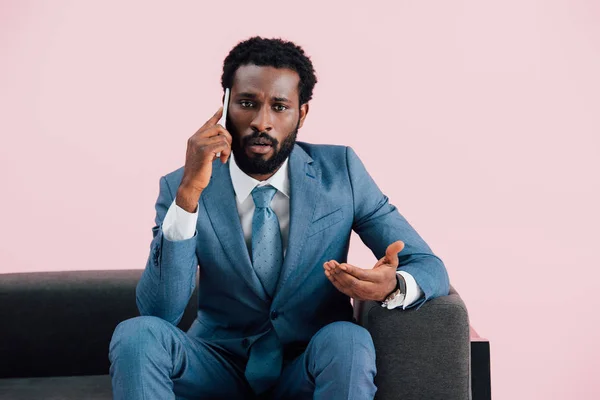 Афроамериканець бізнесмен сидить у кріслі і говорити на смартфоні, ізольований на рожевому — стокове фото