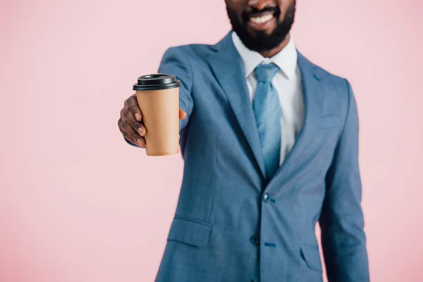 Vista recortada de sonriente hombre de negocios afroamericano sosteniendo café para llevar, aislado en rosa - foto de stock