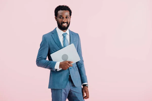 Веселий афроамериканець бізнесмен тримає ноутбук ізольований на рожевому — стокове фото