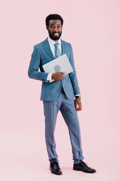 African american businessman holding laptop isolated on pink — стокове фото