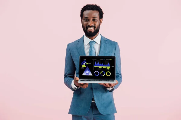 Sonriente hombre de negocios afroamericano mostrando portátil con infografía aislada en azul - foto de stock