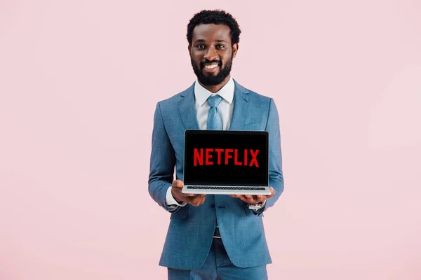 QUIIV, UCRÂNIA - MAIO 17, 2019: sorridente empresário afro-americano mostrando laptop com site da rede, isolado em rosa — Fotografia de Stock