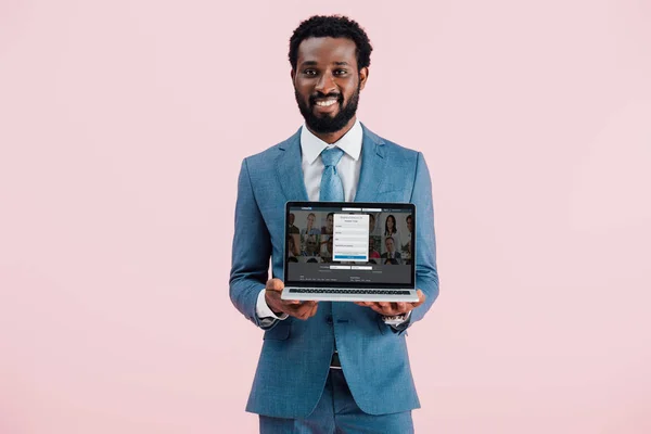 KYIV, UKRAINE - MAY 17, 2019: smiling african american businessman showing laptop with linkedin website, isolated on pink — Stock Photo