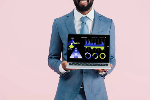 Обрізаний вид усміхненого афроамериканського бізнесмена, що показує ноутбук з інфографікою ізольовано на синьому — стокове фото