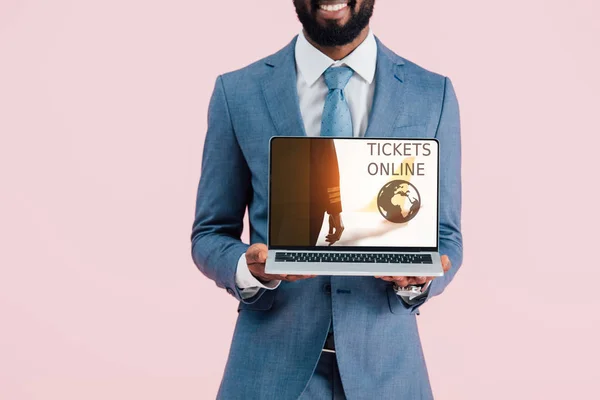 Vista cortada de sorridente empresário afro-americano mostrando laptop com bilhetes site on-line isolado em azul — Fotografia de Stock
