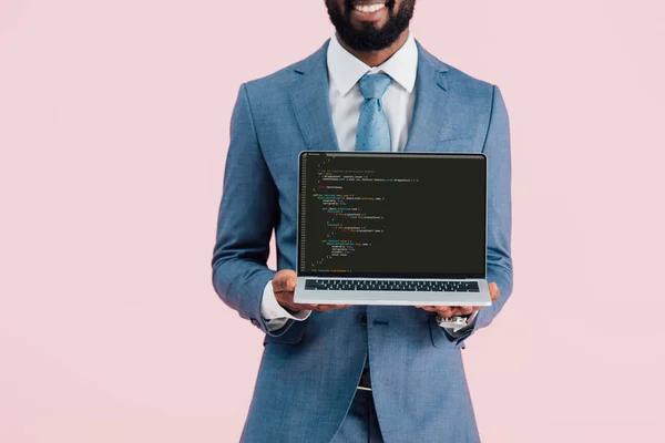 KYIV, UCRANIA - 17 de mayo de 2019: vista recortada de un hombre de negocios afroamericano sonriente mostrando una computadora portátil con código html, aislado en rosa - foto de stock