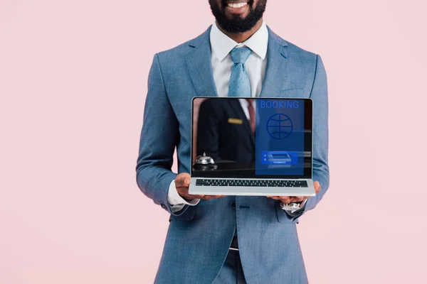Vista ritagliata di sorridente uomo d'affari africano americano mostrando laptop con prenotazione sito web isolato su blu — Foto stock