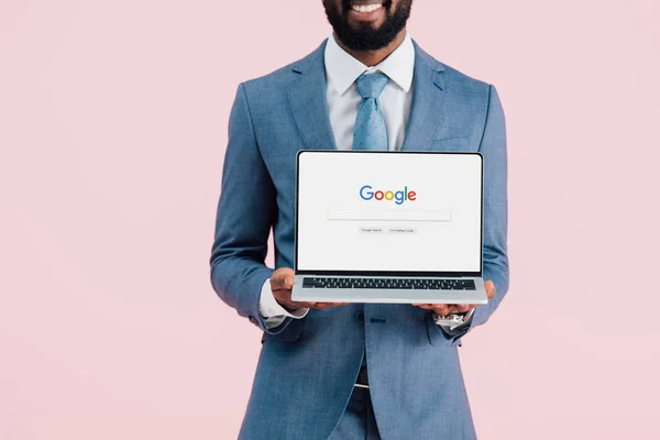 Kyiv, ukraine - 17. Mai 2019: Ausschnitt eines lächelnden afrikanisch-amerikanischen Geschäftsmannes, der einen Laptop mit google-Webseite zeigt, isoliert auf rosa — Stockfoto