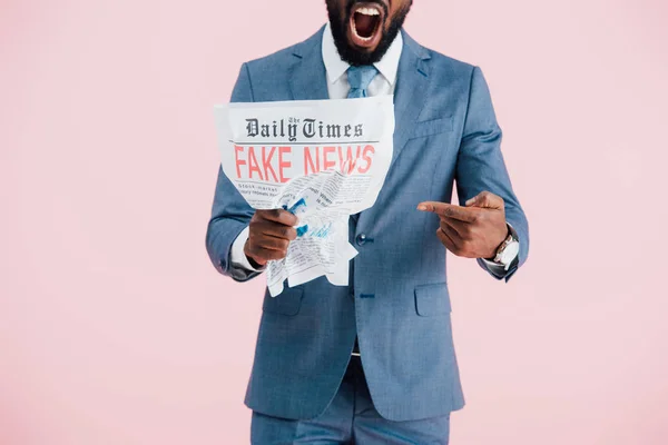 Cropped view of aggressive african american businessman holding newspaper with fake news isolated on pink — Stock Photo