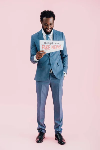 Веселий афроамериканець бізнесмен Редінг газета з підробленими новинами, ізольовані на рожевий — стокове фото