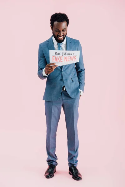 Cheerful african american businessman reading newspaper with fake news isolated on pink — Stock Photo