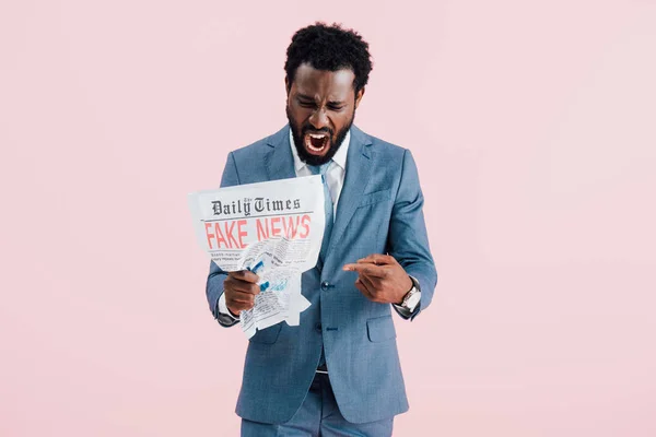 Aggressive african american businessman shouting and reading newspaper with fake news isolated on pink — Stock Photo