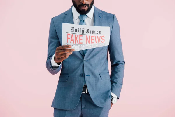 Обрезанный вид африканского американского бизнесмена, читающего газету с фейковыми новостями, изолированными на розовом — стоковое фото