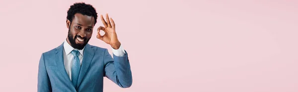 Веселий афроамериканець бізнесмен в костюмі показані OK знак, ізольований на рожевому — стокове фото
