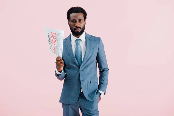 Sad african american businessman holding newspaper with fake news isolated on pink — Stock Photo