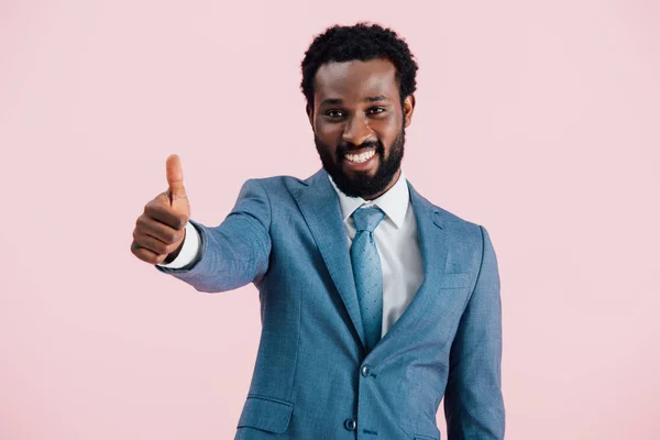 Sonriente hombre de negocios afroamericano en traje mostrando el pulgar hacia arriba, aislado en rosa - foto de stock